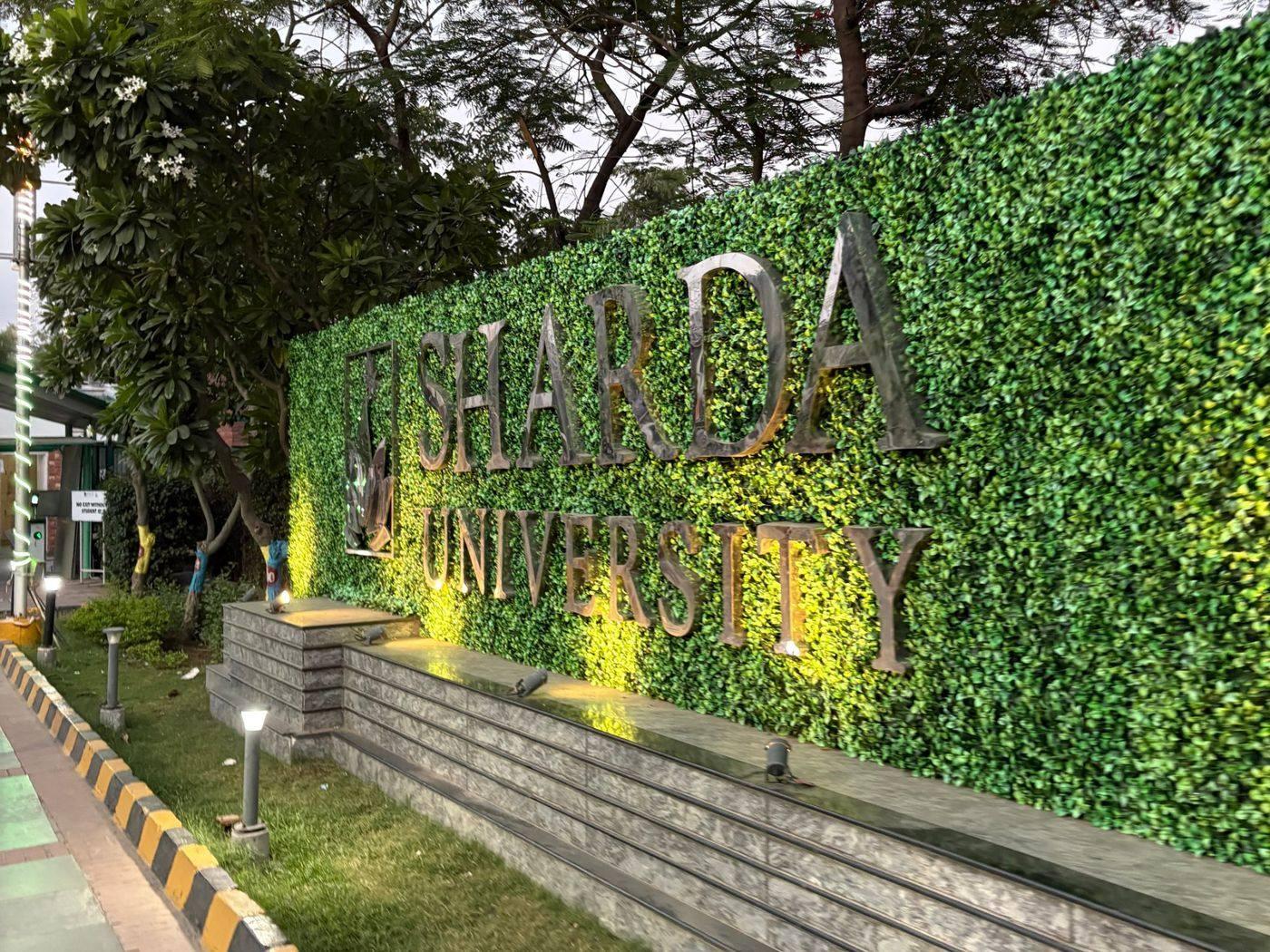 সবুজ পাতার দেয়ালে Sharda University লেখা নামফলক