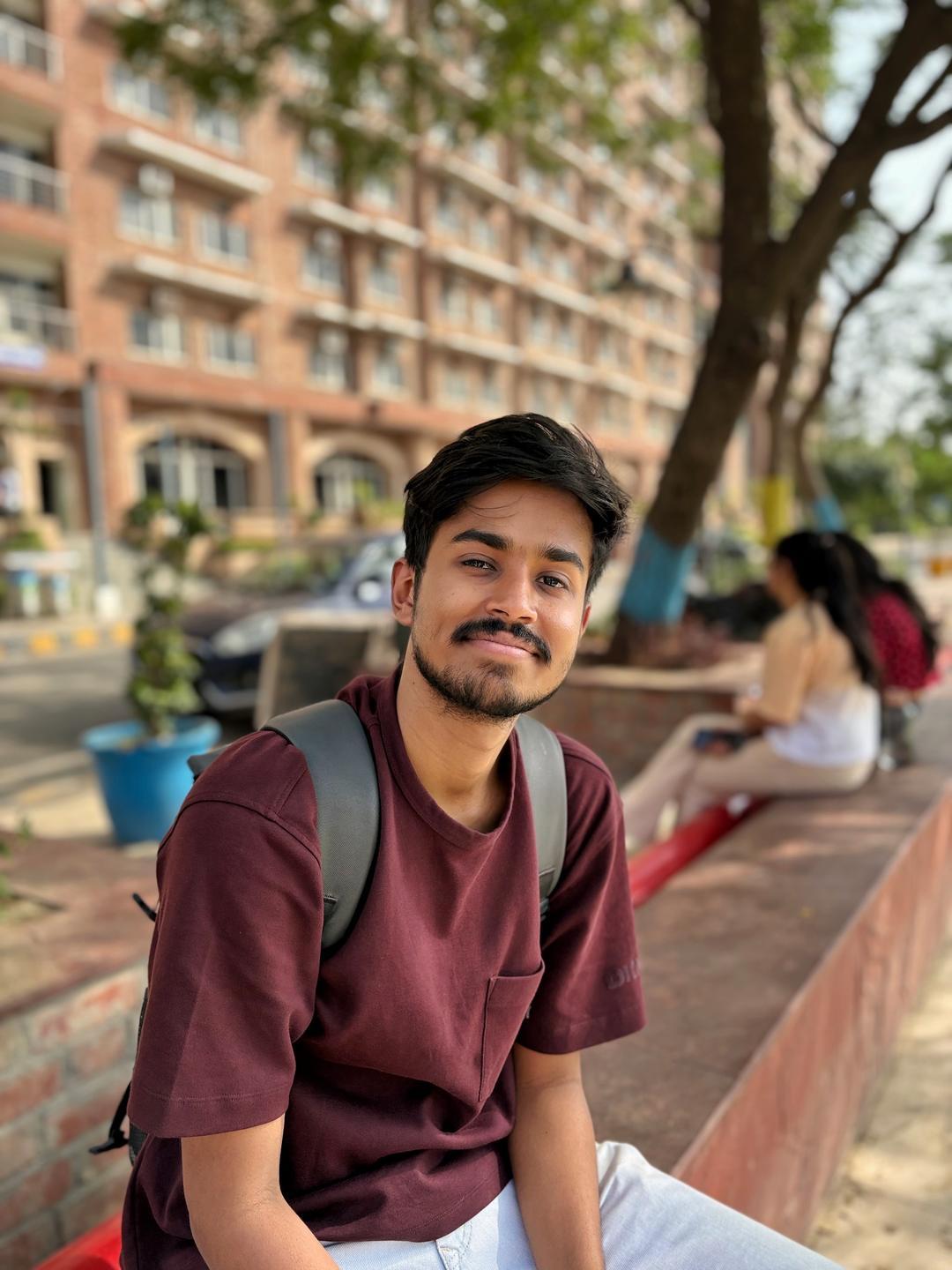 কাঁধে ব্যাগ নিয়ে ক্যাম্পাসে বসে হাসছেন মৃণাল দাস
